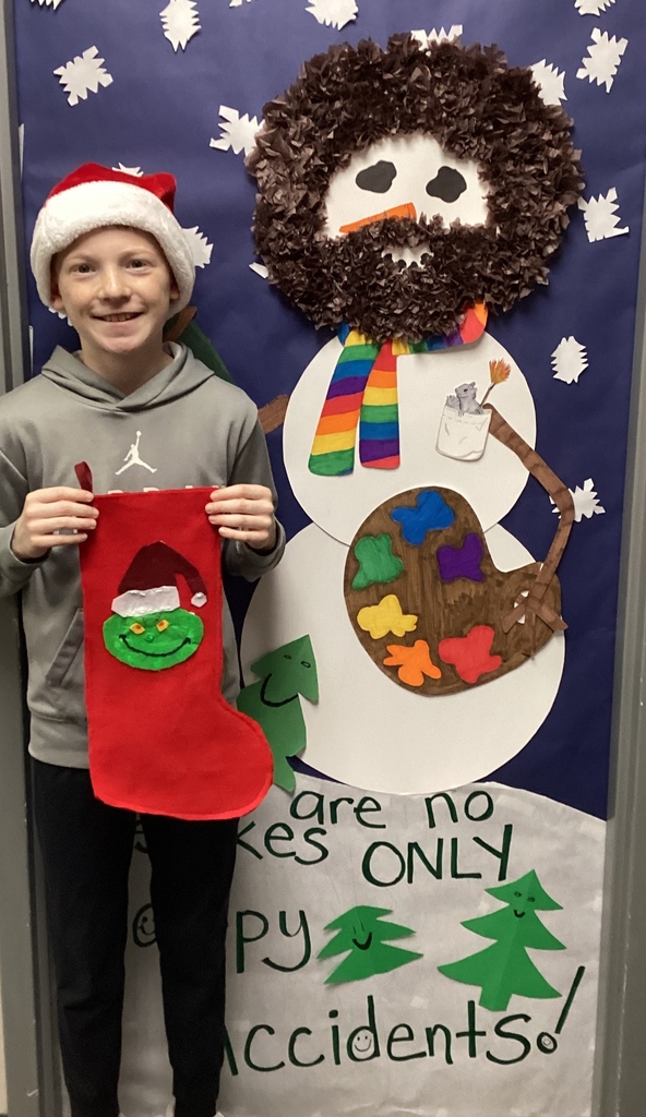 Student standing in front of a door that is covered by an artist snowman holding a red stocking with a Grinch.