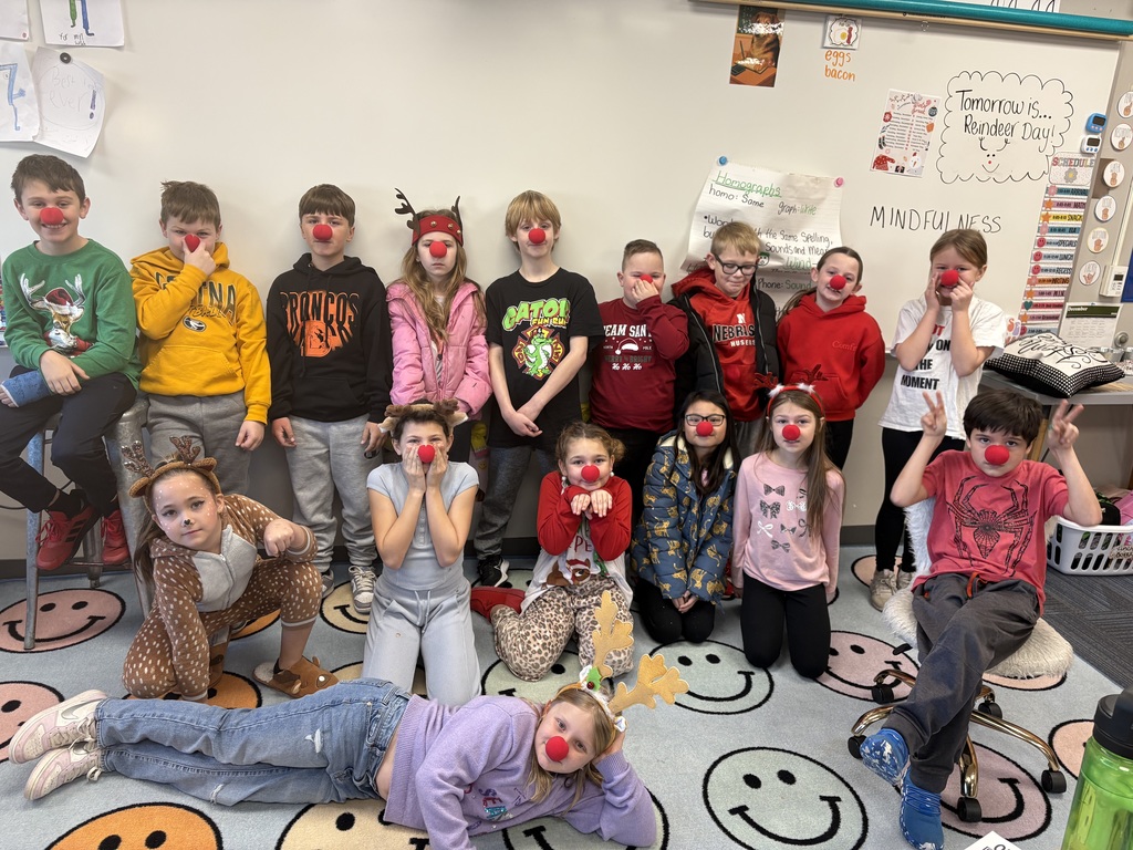 Group of students standing and kneeling for a picture in front a whiteboard wearing reindeer gear.