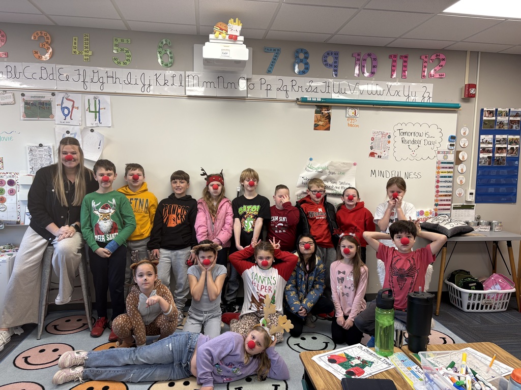 Group of students standing and kneeling for a picture in front a whiteboard wearing reindeer gear.