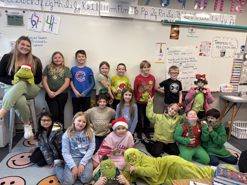 Group of students standing and kneeling for a picture in front a whiteboard wearing grinch gear.