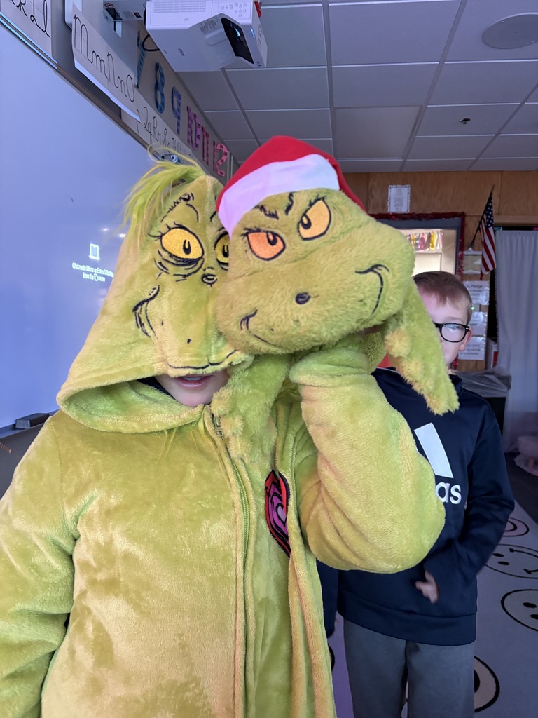 One student wearing a grinch costumer while holding a grinch head.