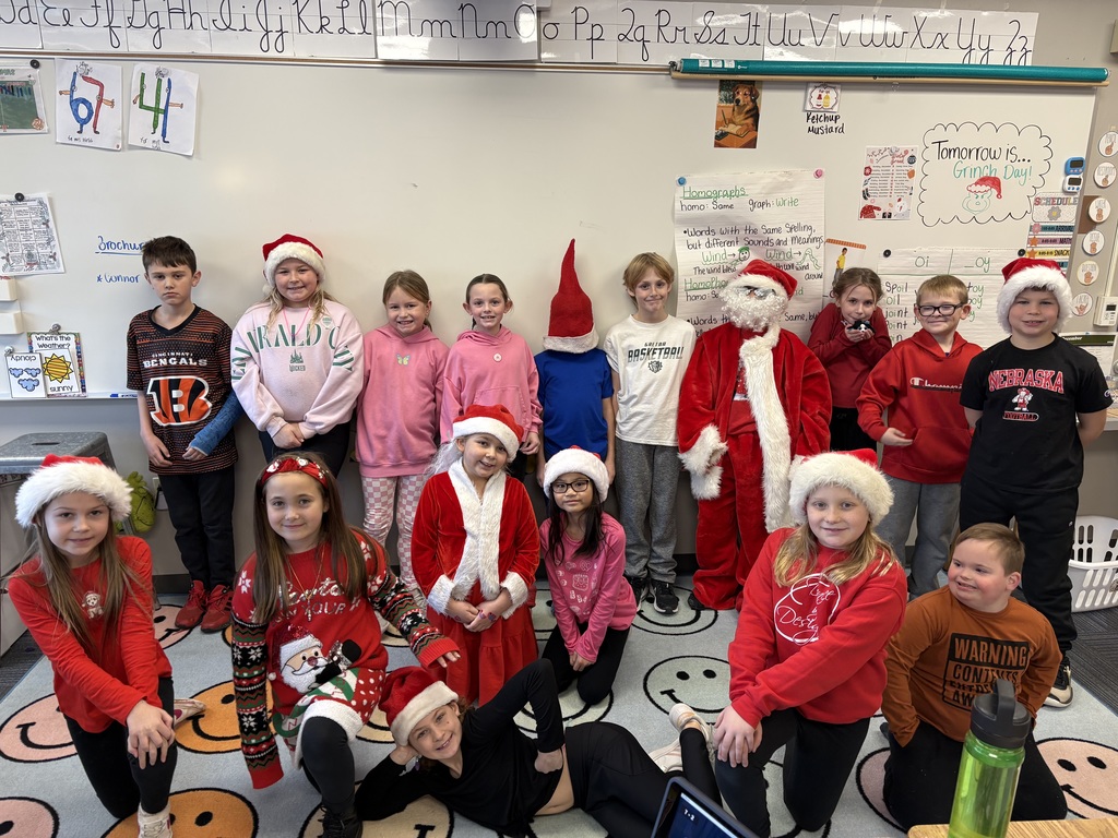 Group of students standing and kneeling for a picture in front a whiteboard wearing red Christmas gear.