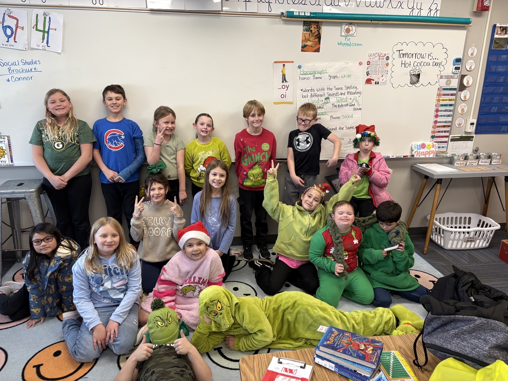 Group of students standing and kneeling for a picture in front a whiteboard wearing grinch gear.