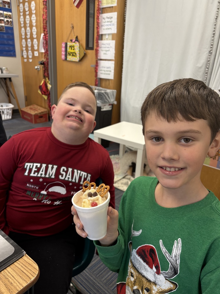 Two boys smile at desks with a cup with a reindeer dessert inside.