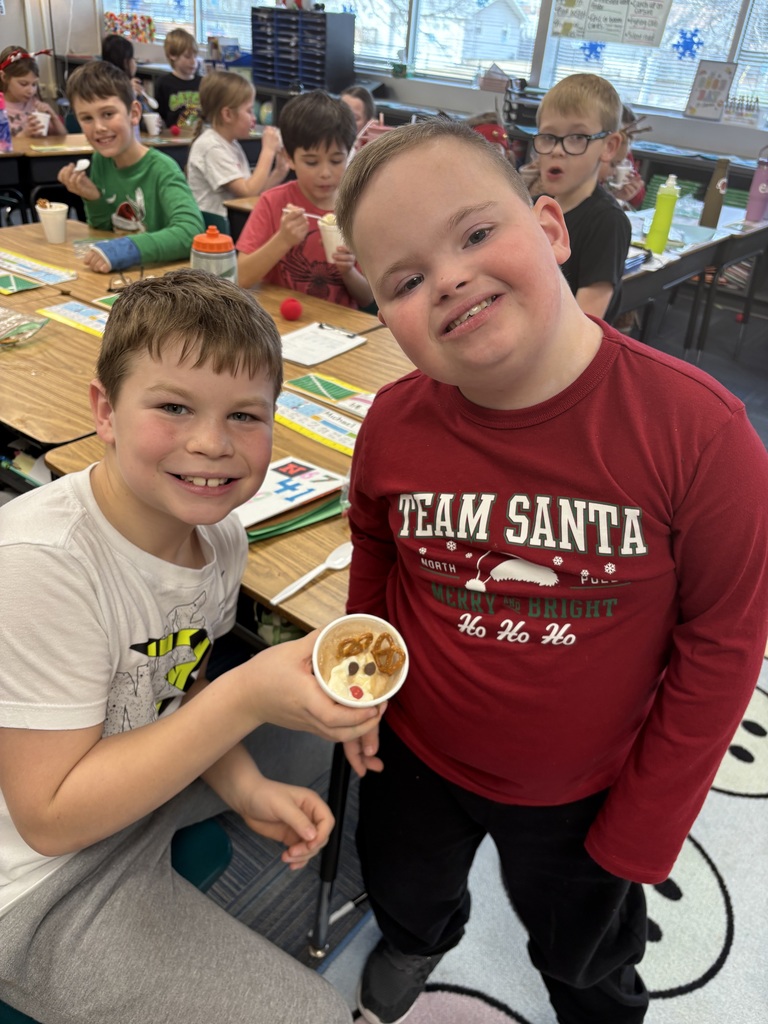 Two boys smile at desks with a cup with a reindeer dessert inside.