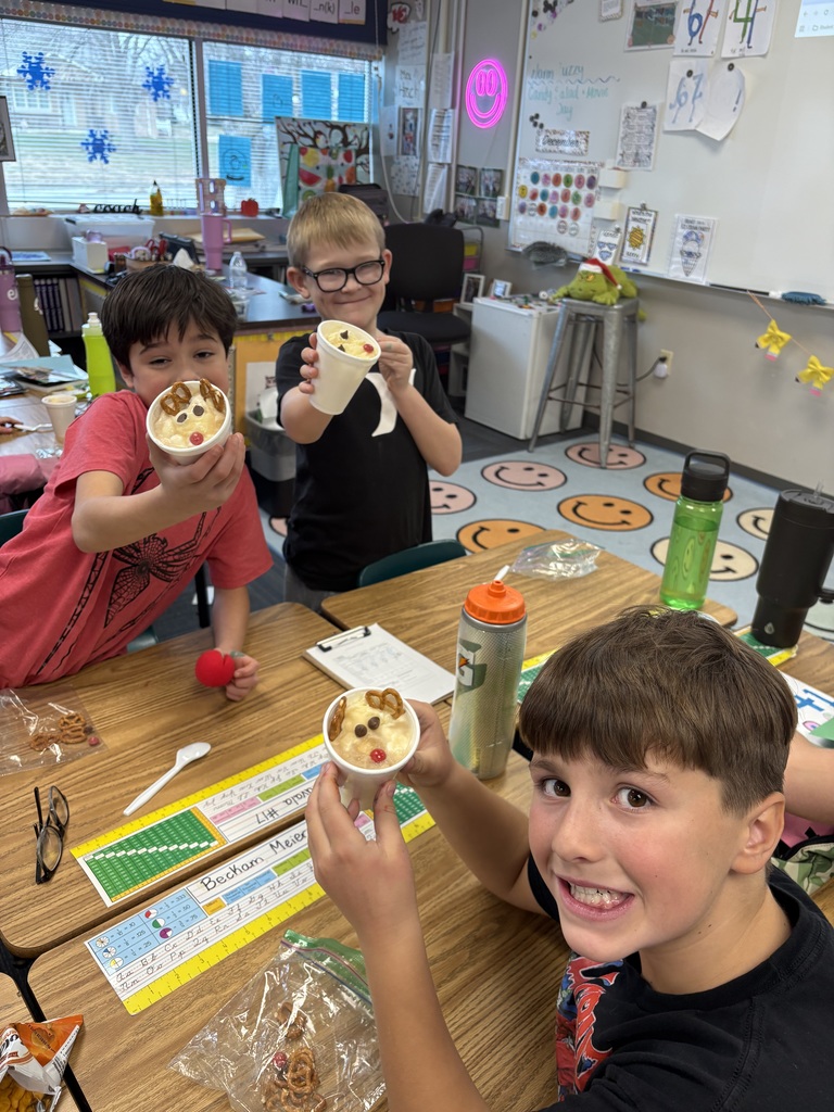 Three boys smile at desks with a cup with a reindeer dessert inside.