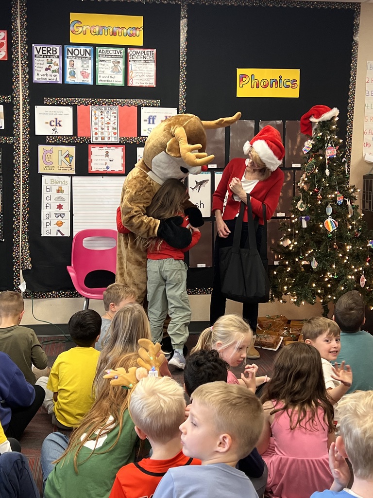 A girl hugs a person dressed in a Rudolph costume while a woman with a Santa hat looks on.