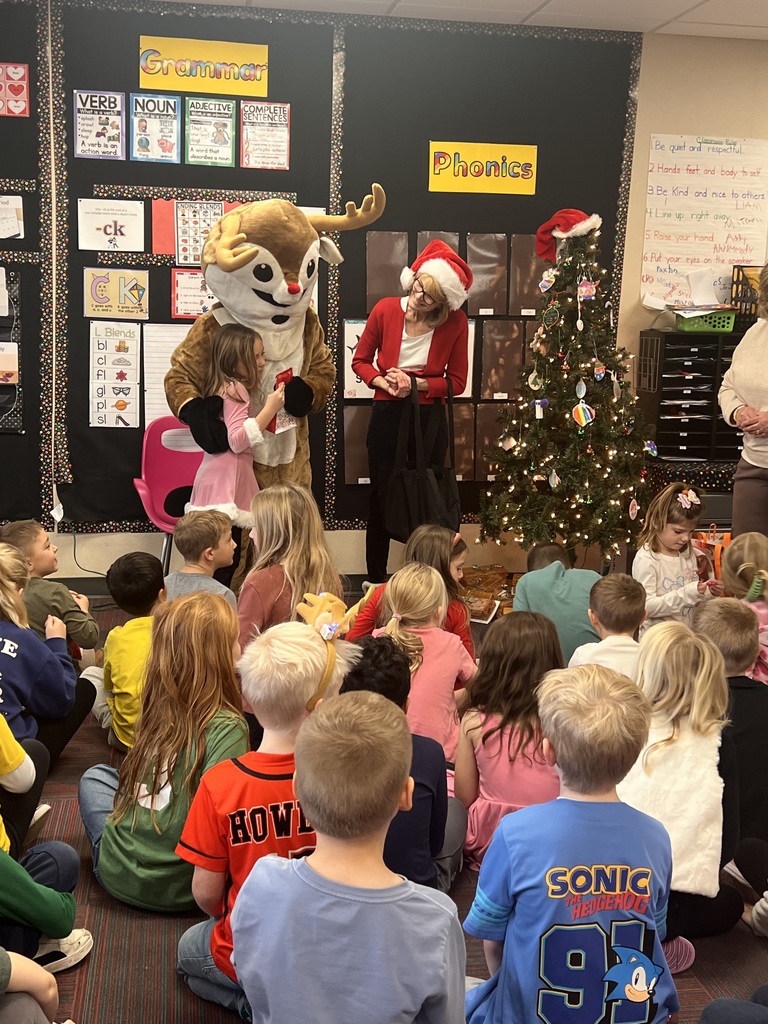 A girl hugs a person dressed in a Rudolph costume while a woman with a Santa hat looks on.