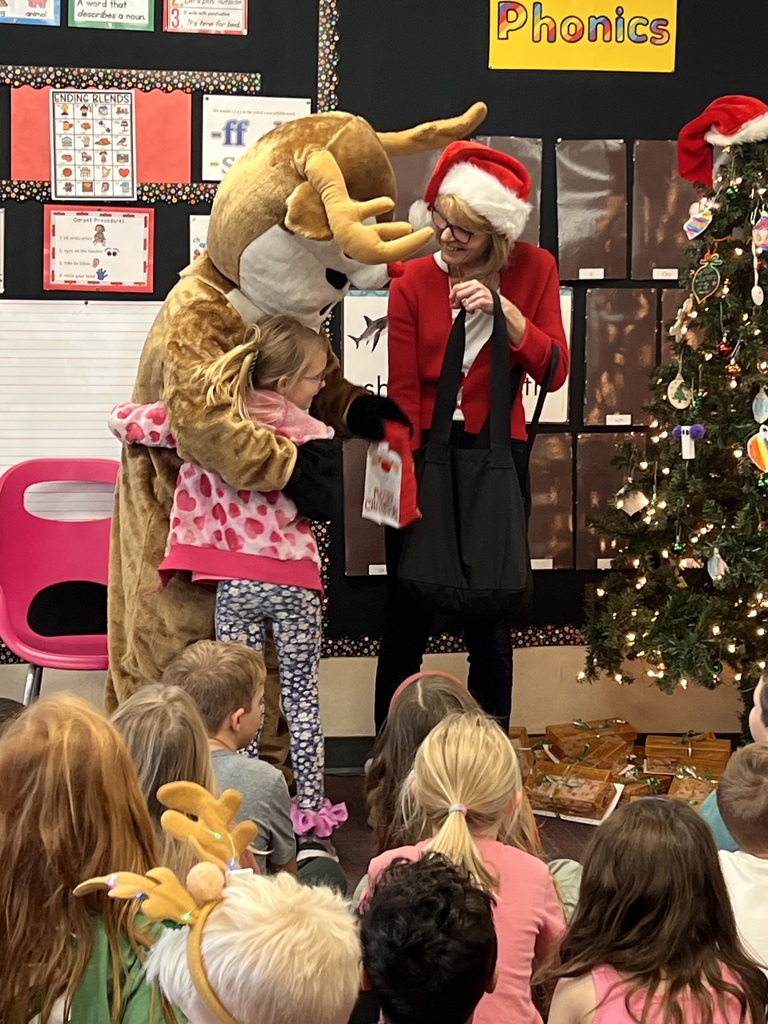 A girl hugs a person dressed in a Rudolph costume while a woman with a Santa hat looks on.