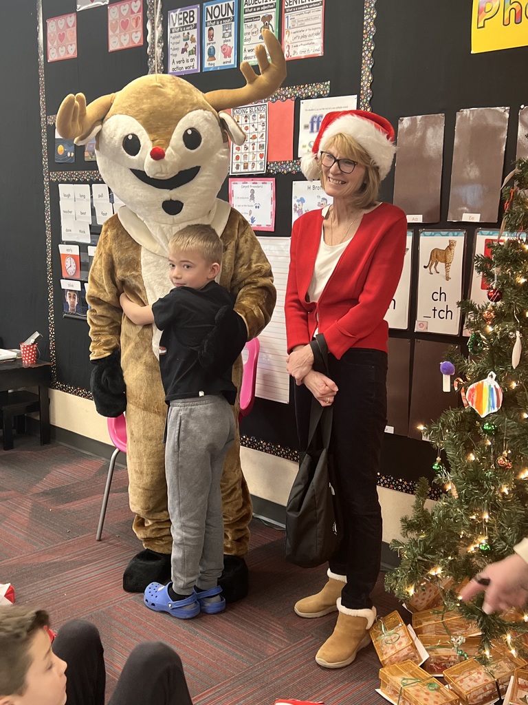 A boy hugs a person dressed in a Rudolph costume while a woman with a Santa hat looks on.