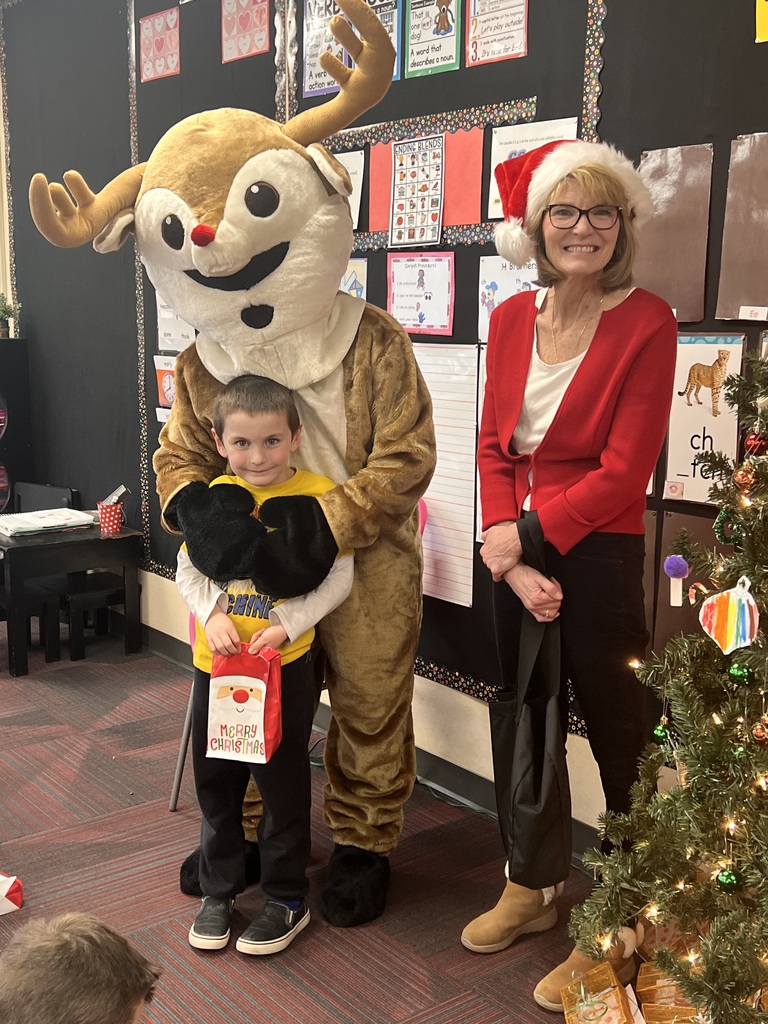 A boy hugs a person dressed in a Rudolph costume while a woman with a Santa hat looks on.