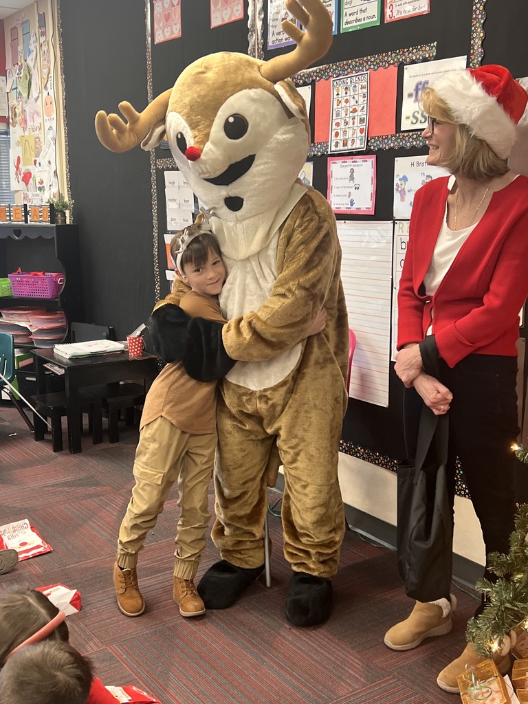 A boy hugs a person dressed in a Rudolph costume while a woman with a Santa hat looks on.