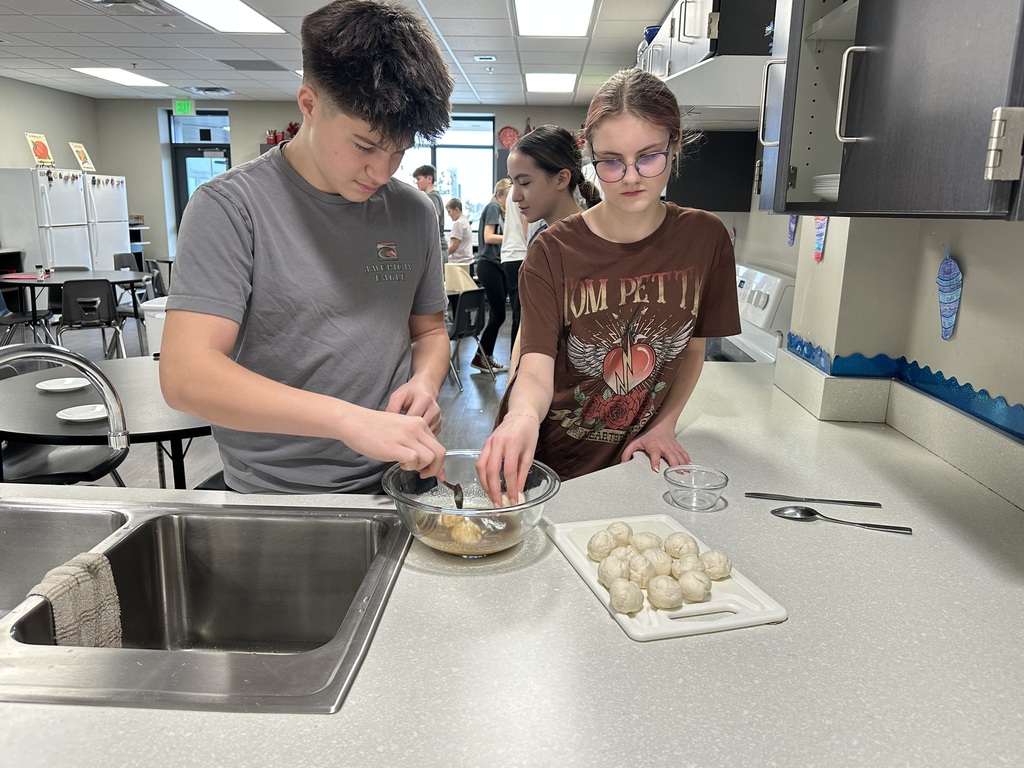 Photo of a male student and a female students dropping chunks of biscuit dough into a cinnamon sugar mixture.