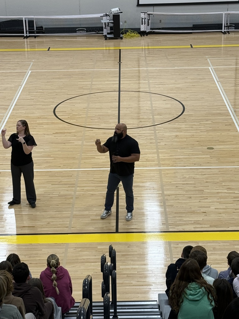 Coach Mackey and an ASL interpreter speak to students in a gym.