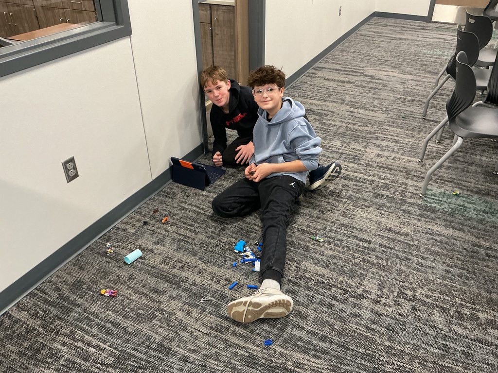 Two boys sit on the floor with their ipad and toys working on a project. 