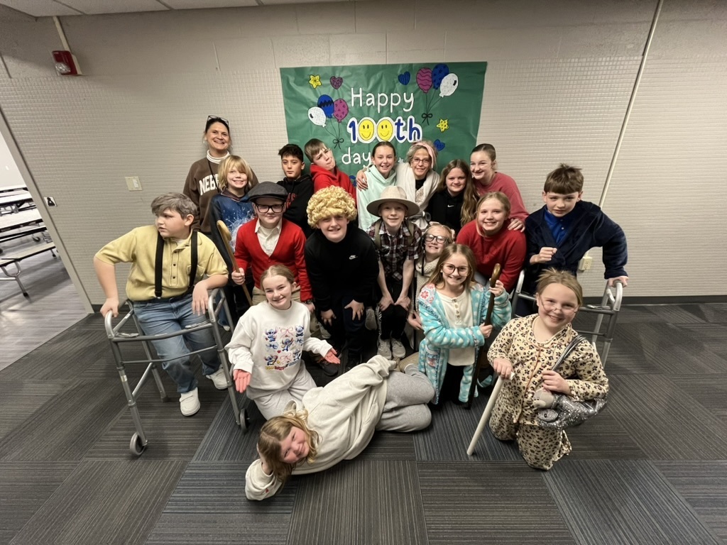 Group of students, some dressed really old with their teacher standing in front of a 100th day of school sign