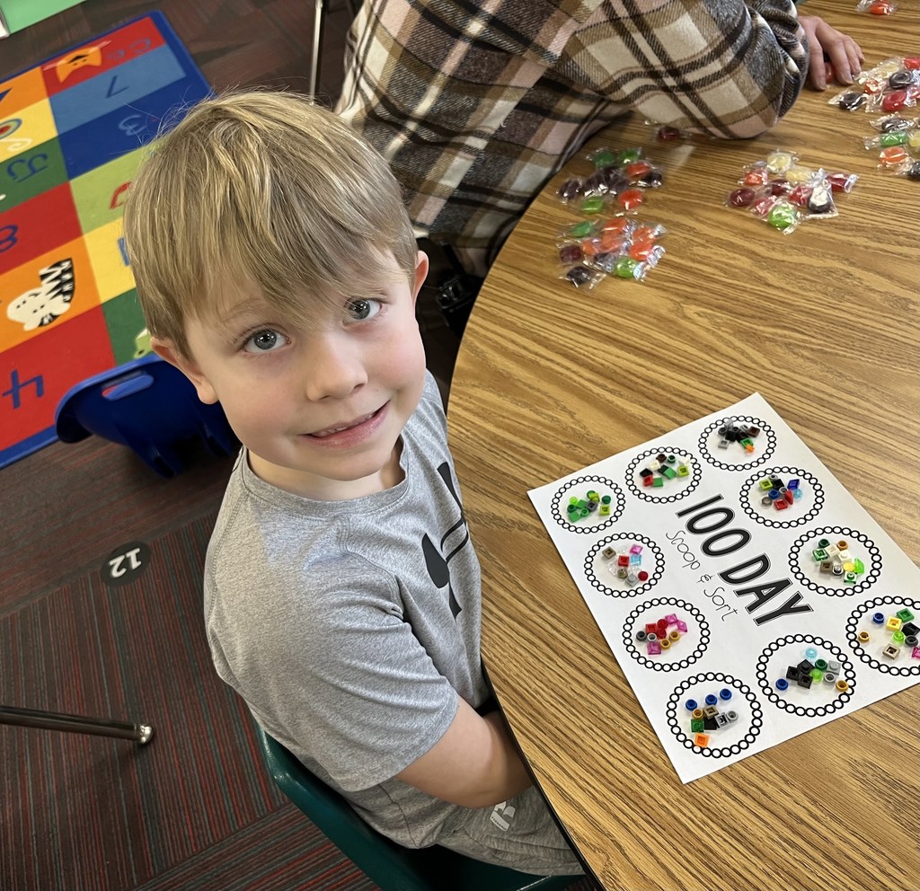 Boy sitting at a table with a 100 day scoop and sort on table