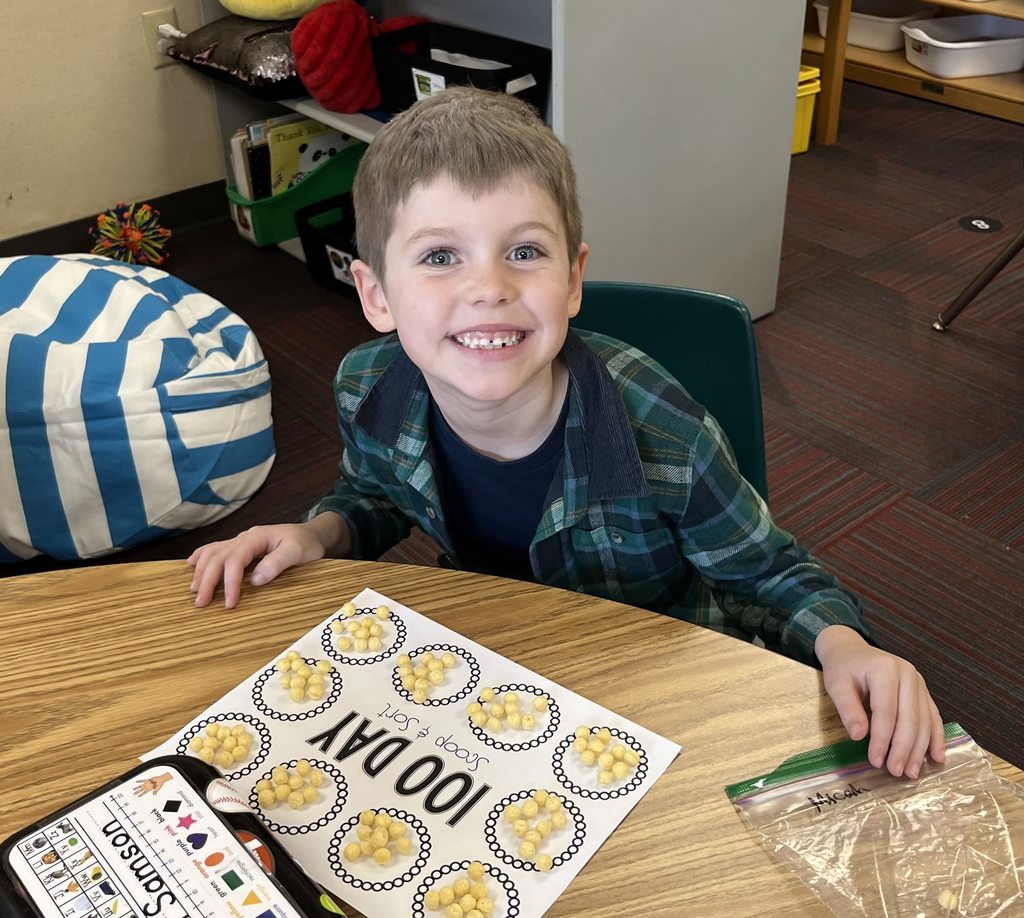 Boy sitting at a table with a 100 day scoop and sort on table