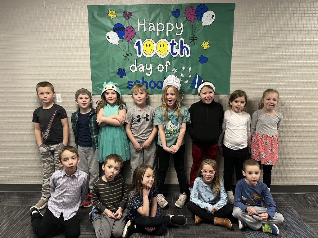 Group of students, some standing and some sitting around a sign that says 100th day of school