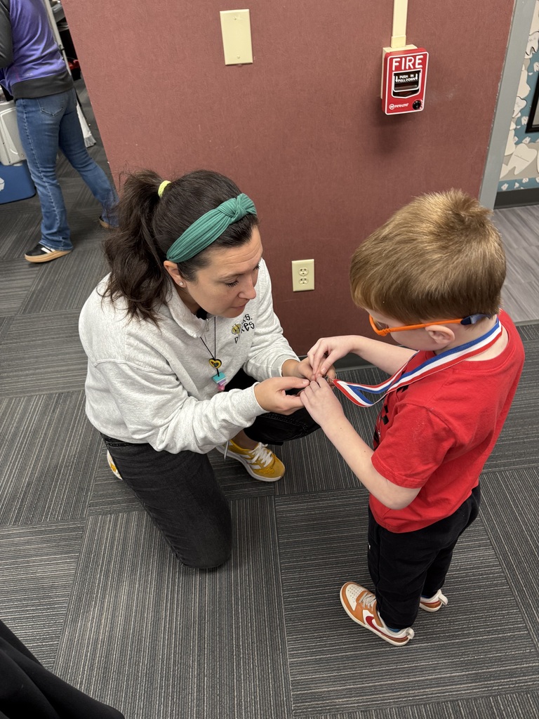 Student shows a woman a medal in front of a red wall.