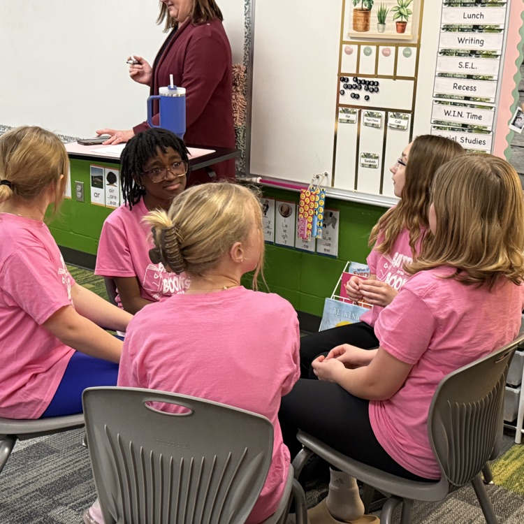 5 girls in pink shirts sit together deciding on an answer  