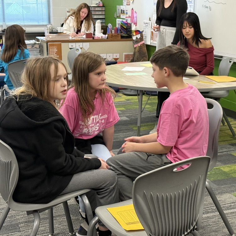 3 kids in pink shirts sit together deciding on an answer. 
