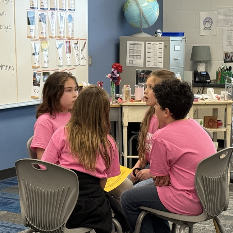 4 kids in pink shirts sit  together deciding on an answer. 