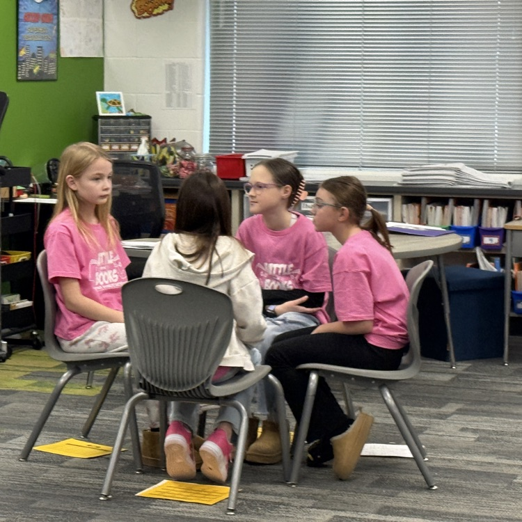 4 girls in pink shirts sit together deciding on an answer. 