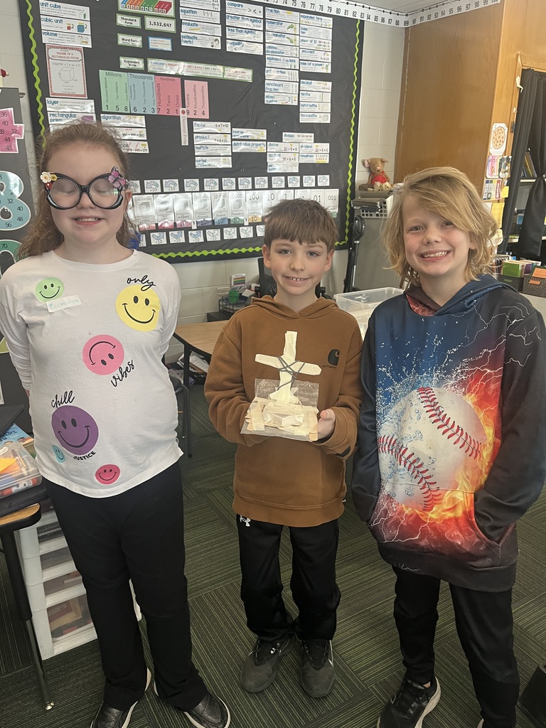 Two boys and a girl standing and holding a craft made out of popsicle sticks.