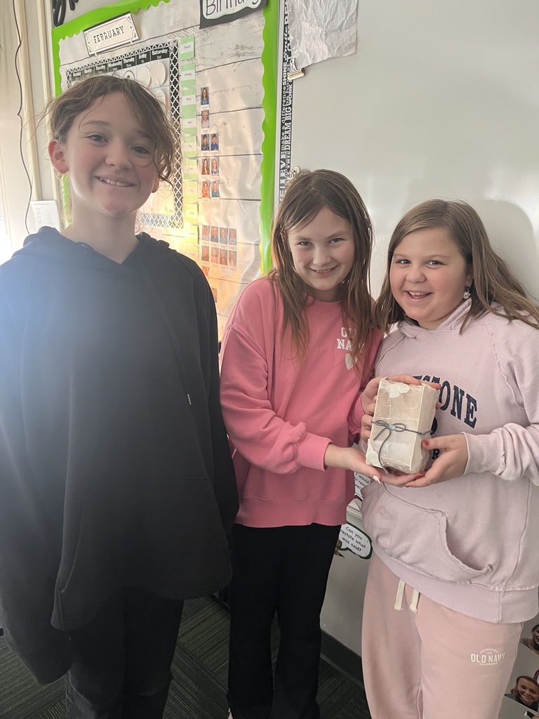 Three girls standing in front of a classroom holding a craft