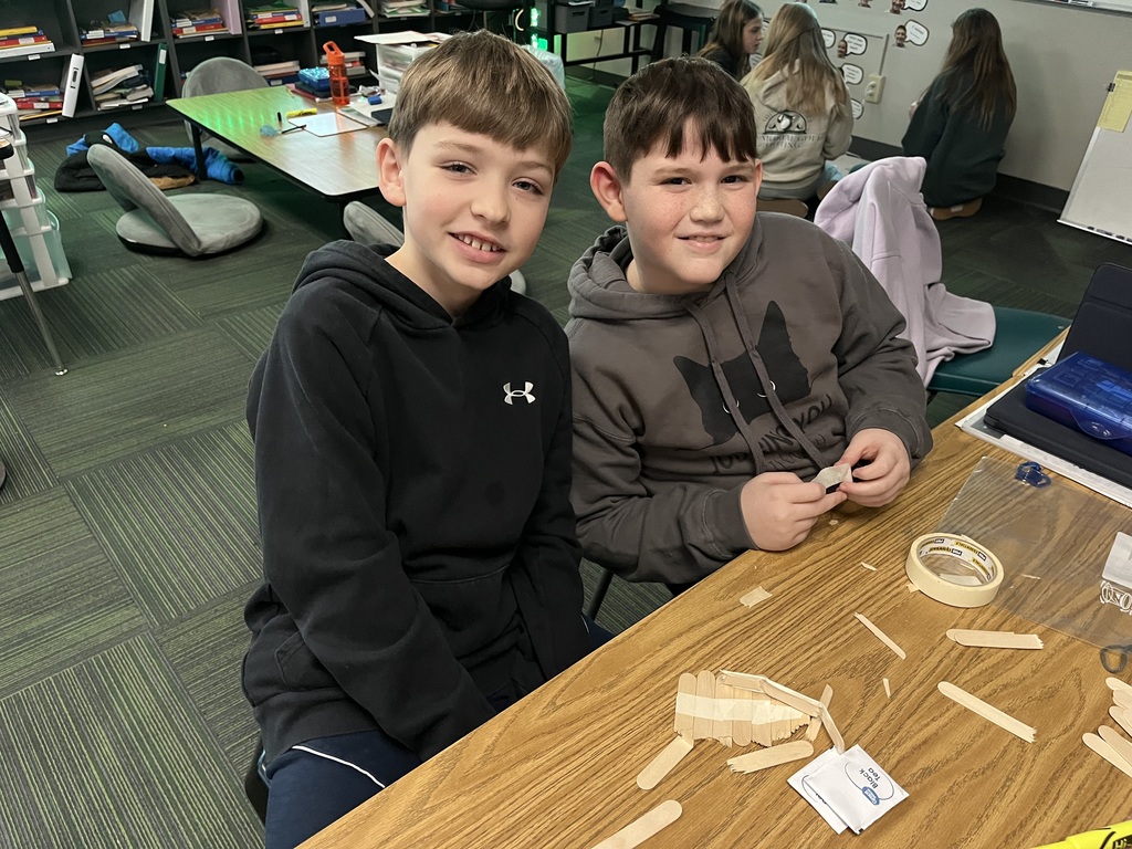 Two boys sitting at a table working on a craft made out of popsicle sticks.
