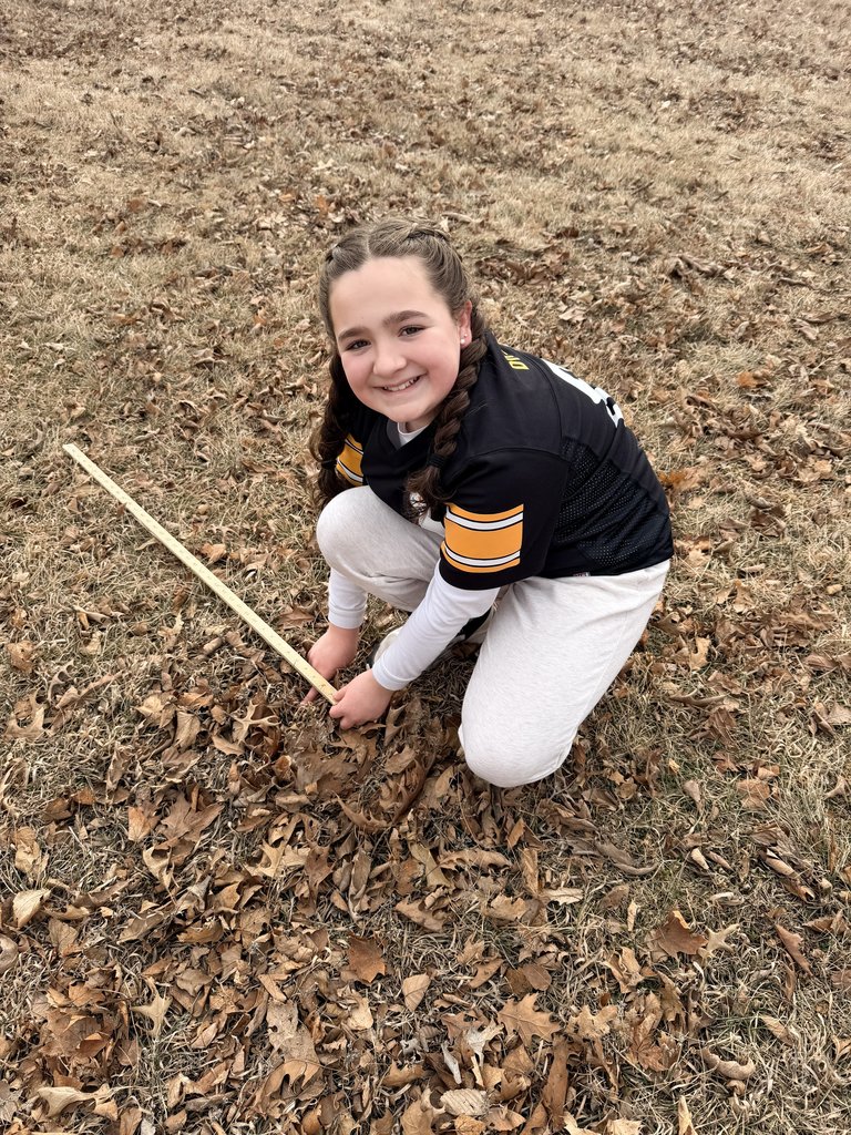 Girl kneeling outside with a jersey on holding a yardstick