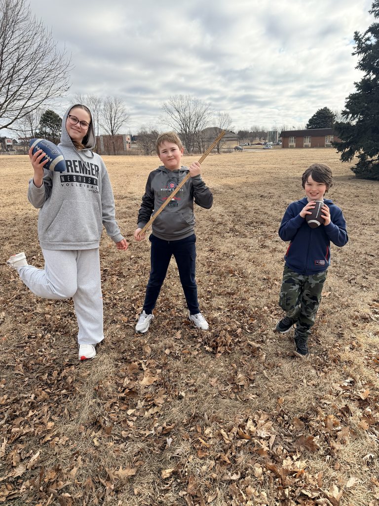 Three students standing outside on a playground holding a yardstick and footballs