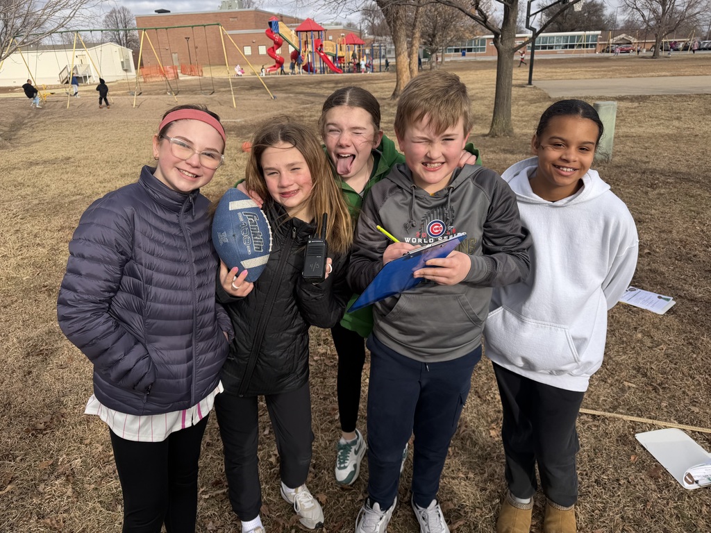 Four girls and one boy standing outside holding a football and a notebook
