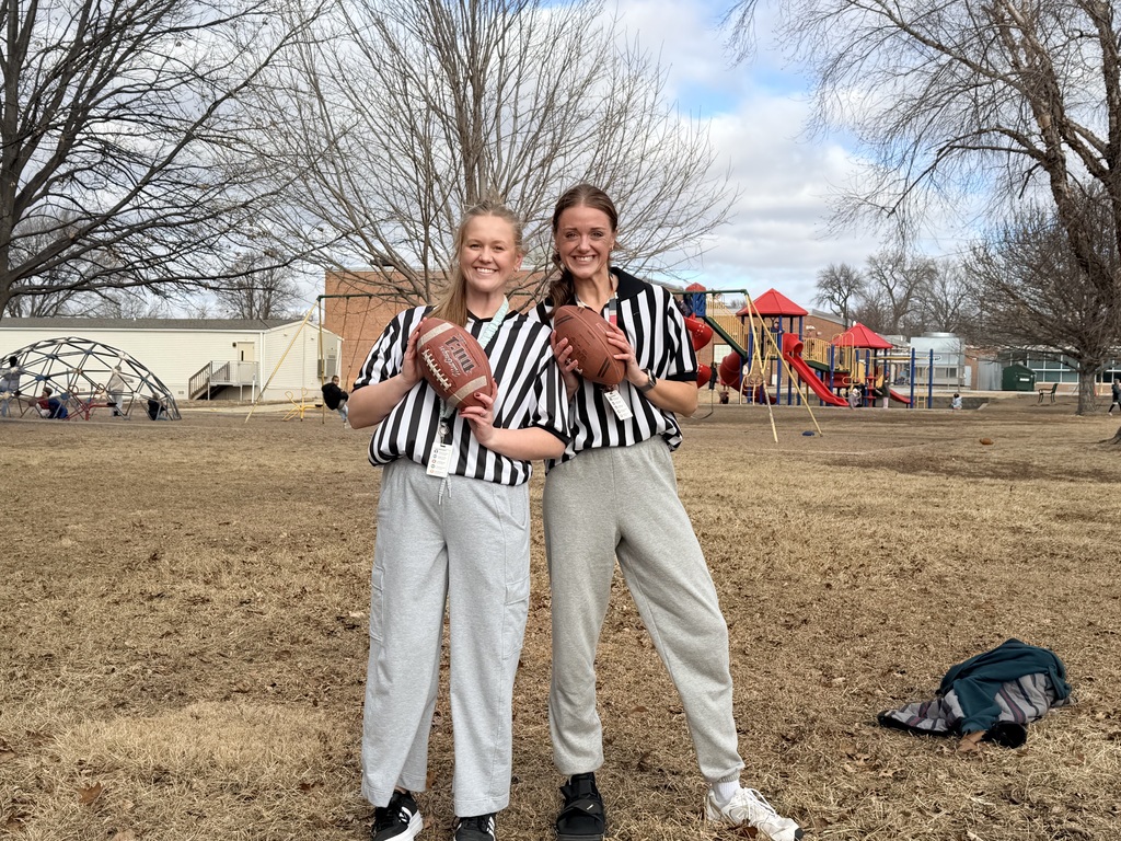 Two adult women standing outside wearing ref clothes holding footballs
