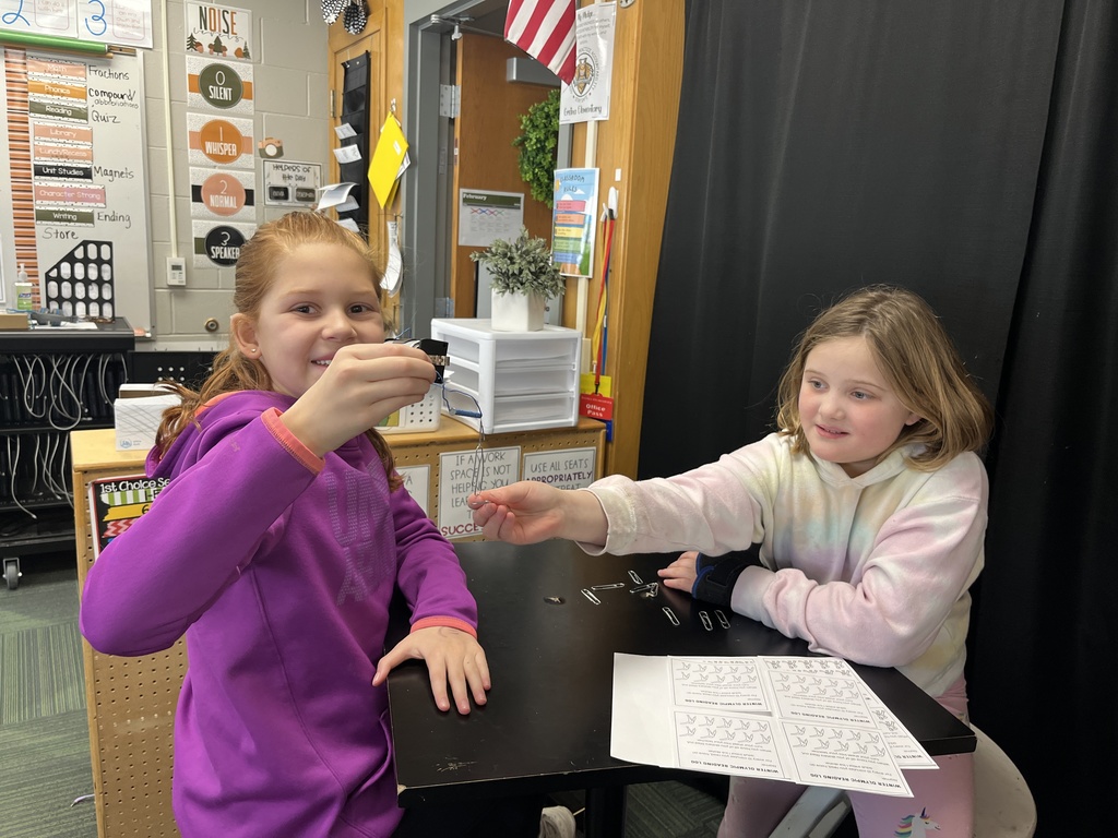 Two girls sitting at a table with worksheets in front of them holding a magnet