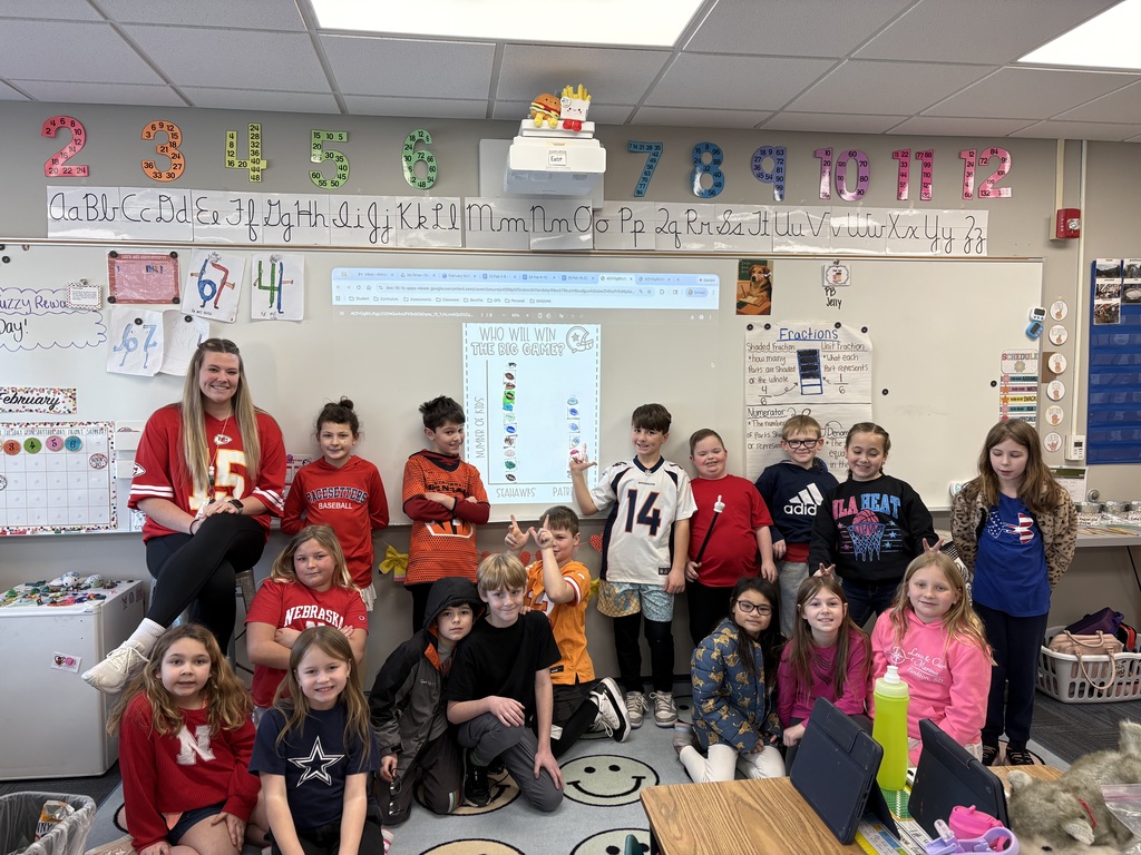 Group of students standing and sitting around a whiteboard wearing jerseys and team shirts