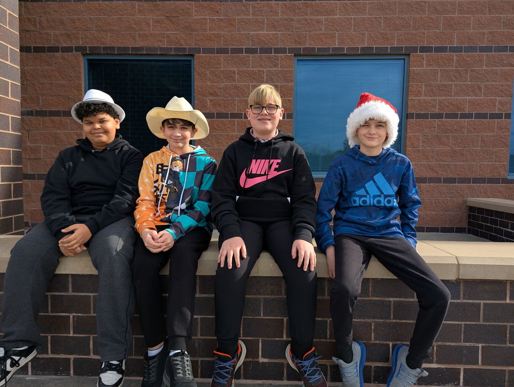 Four male students sit on a concrete ledge. Three of them are wearing hats. 