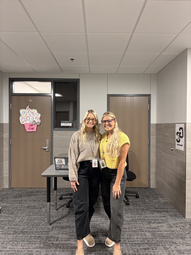 Two female teachers stand together in front of a door. 