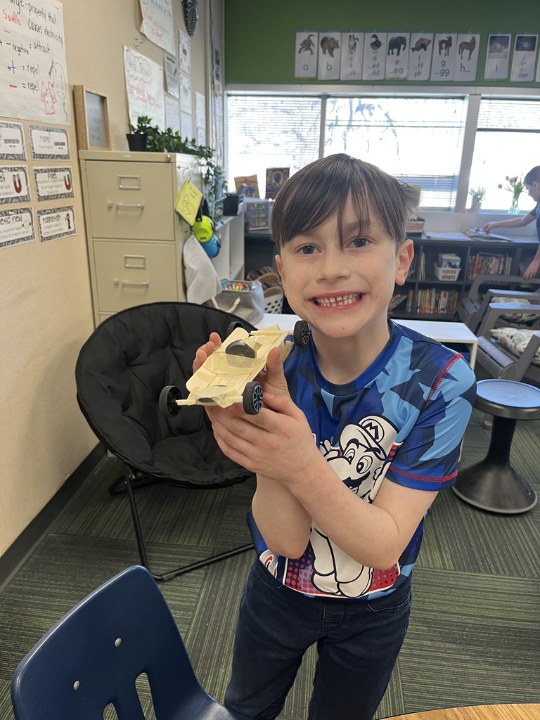Boy holding a car made out of popsicle sticks and tape smiling