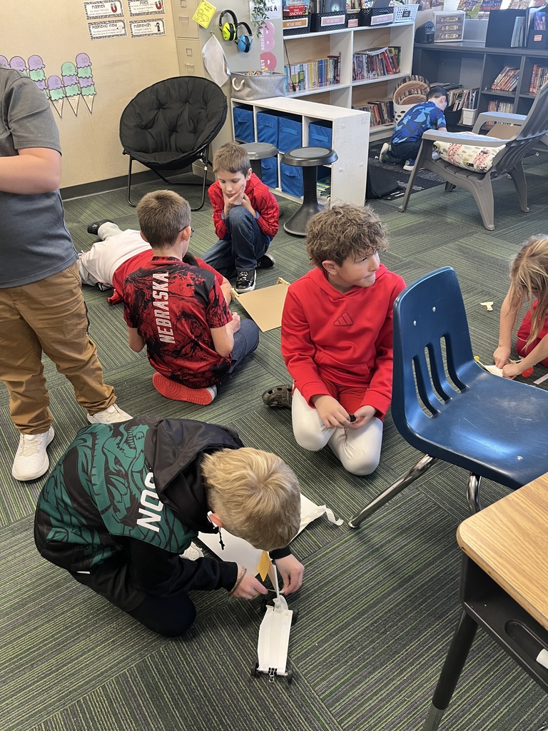 Group of students working in a classroom on cars made out of paper and tape