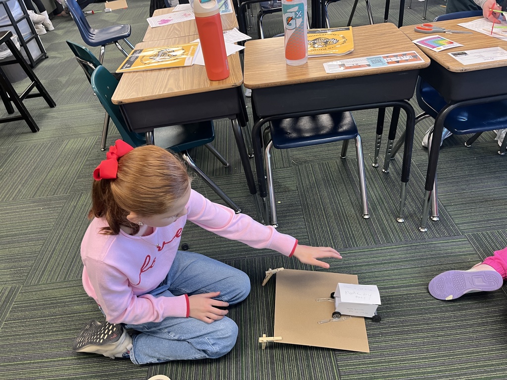 Girl pushes a car made out of note cards and paper clips on a cardboard ramp