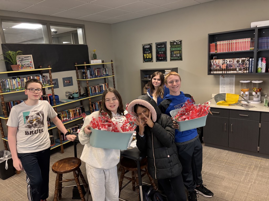 Five students in a classroom smiling and holding totes of Valentine's they made for Hillcrest residents.