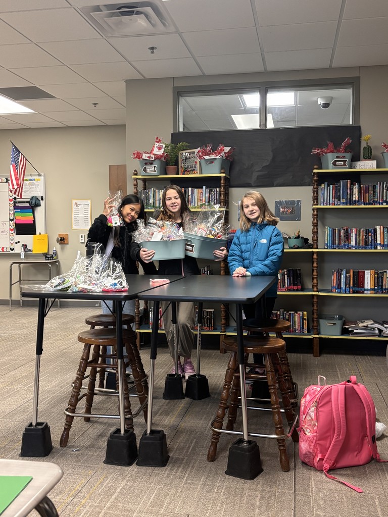 Three students standing at a table in the classroom making Valentine's and putting them in totes.