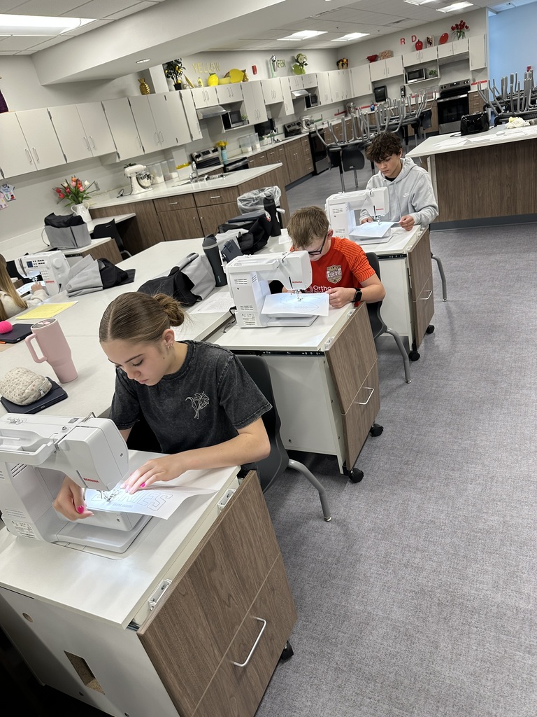 Three students sit at sewing machines and are sewing. 