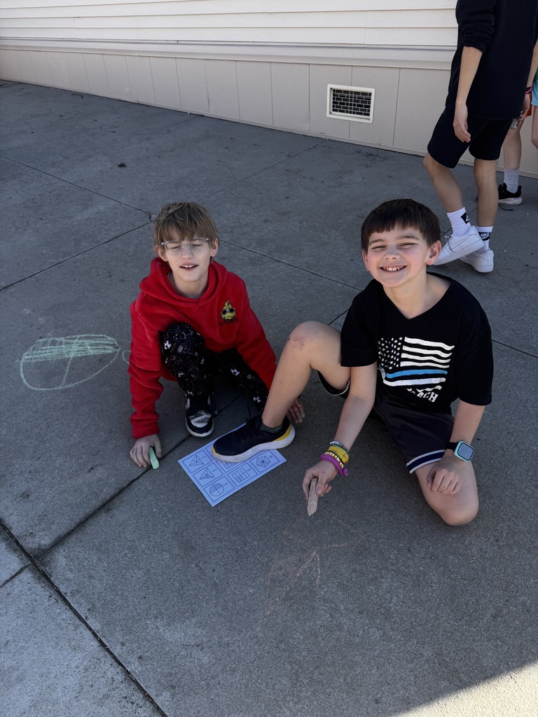 Group of kids on the ground smiling while chalk drawings show on the cement.