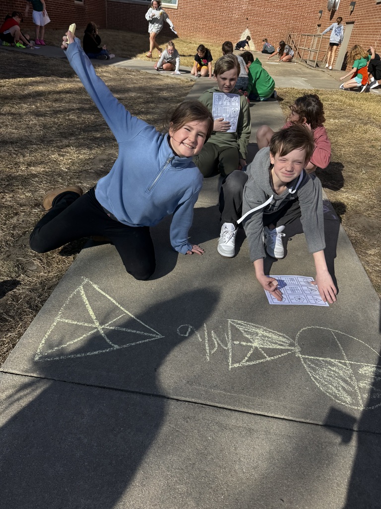 Group of kids on the ground smiling while chalk drawings show on the cement.