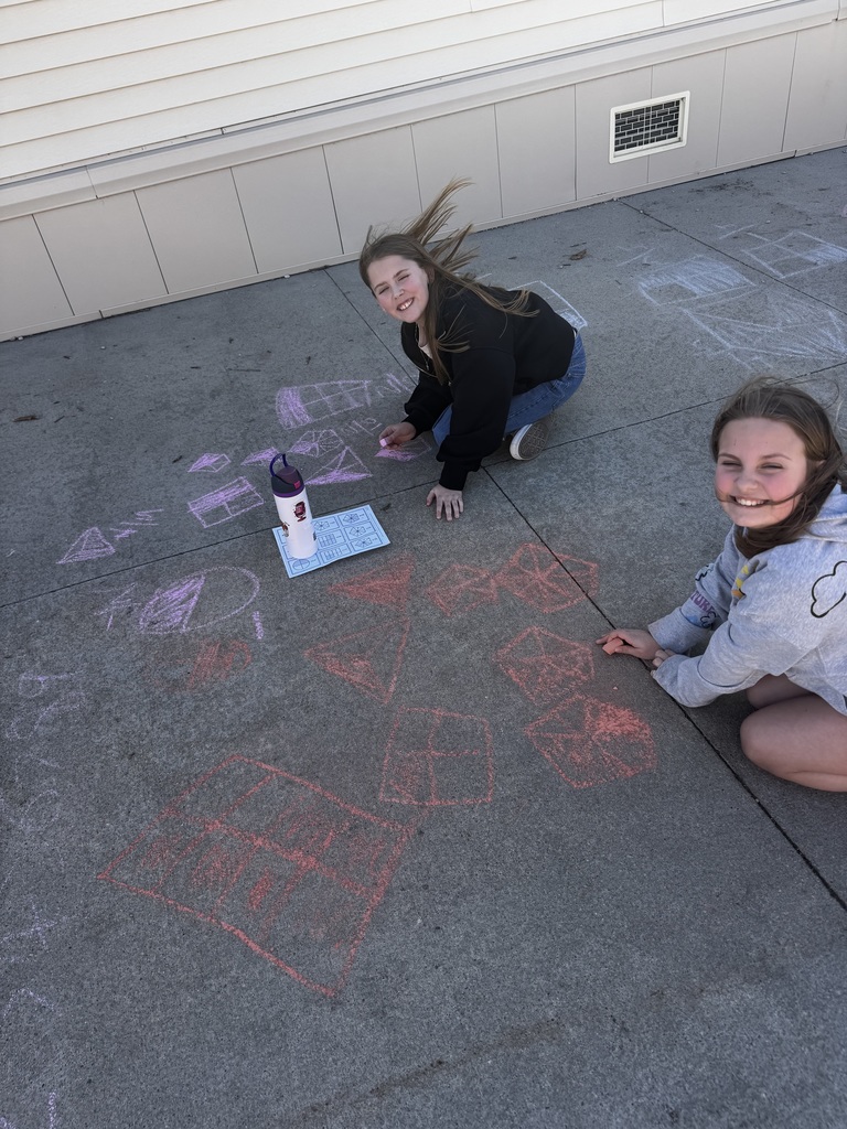Two girls on the ground smiling while chalk drawings show on the cement.