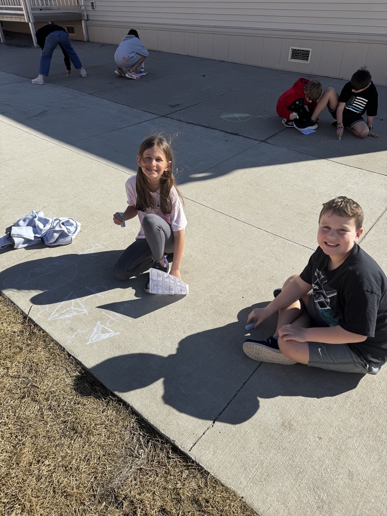 Group of kids on the ground smiling while chalk drawings show on the cement.