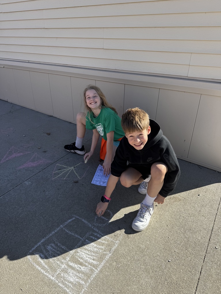 A boy and a girl on the ground smiling while chalk drawings show on the cement.